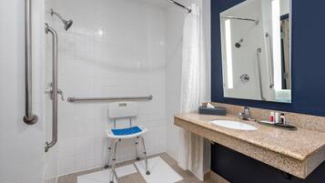 A bathroom with a wheelchair-accessible shower, a sink, and a mirror.