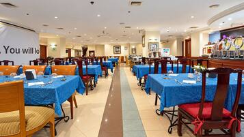 A hotel dining area with multiple tables and chairs, a reception desk, and a banner.