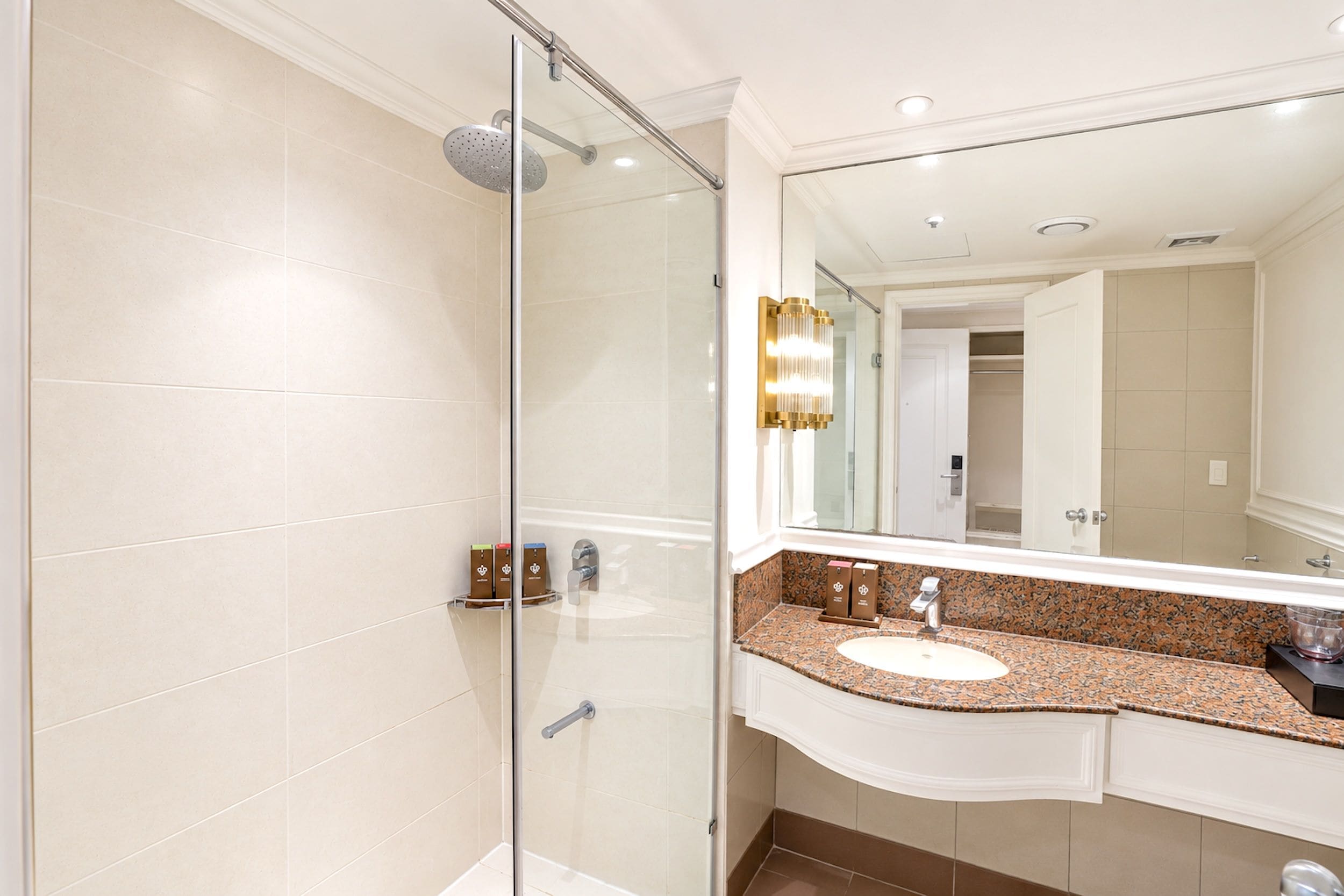 A modern bathroom with a glass shower enclosure, a vanity with a granite countertop, and a large mirror.