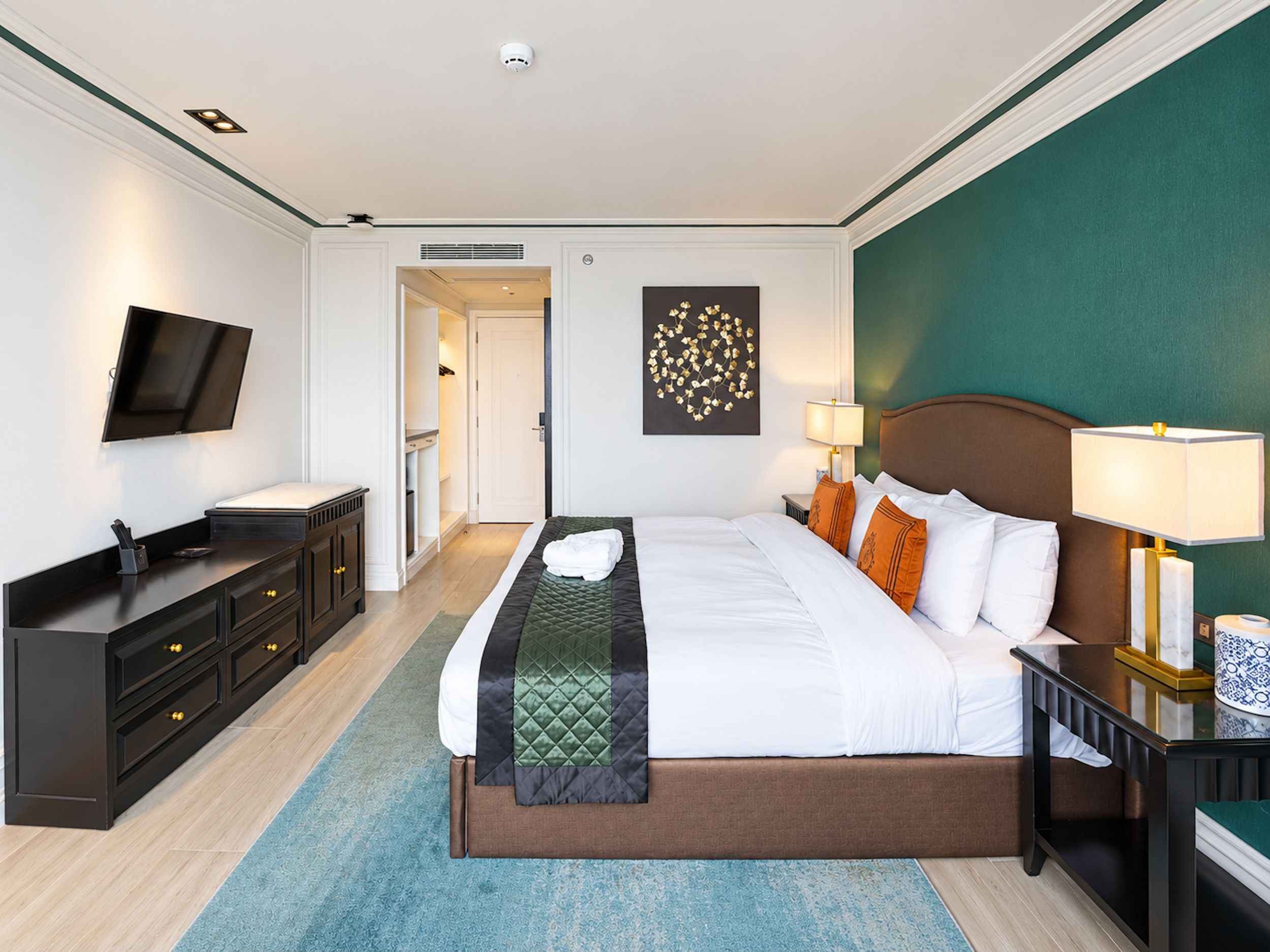 A hotel room with a bed, bedside tables, a TV, a desk, and a wardrobe.