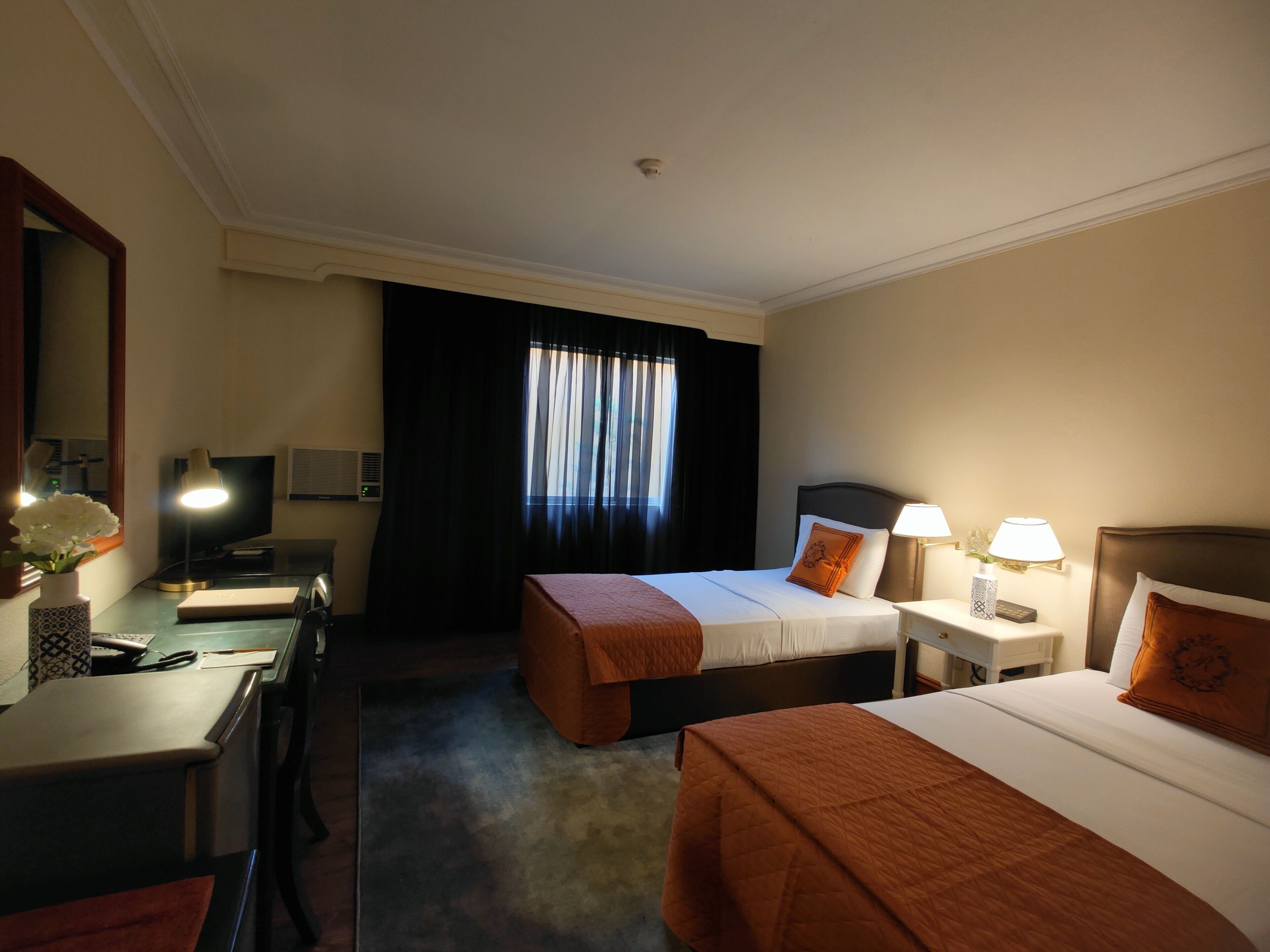 A hotel room with two beds, a desk, a chair, a lamp, and a window with curtains.