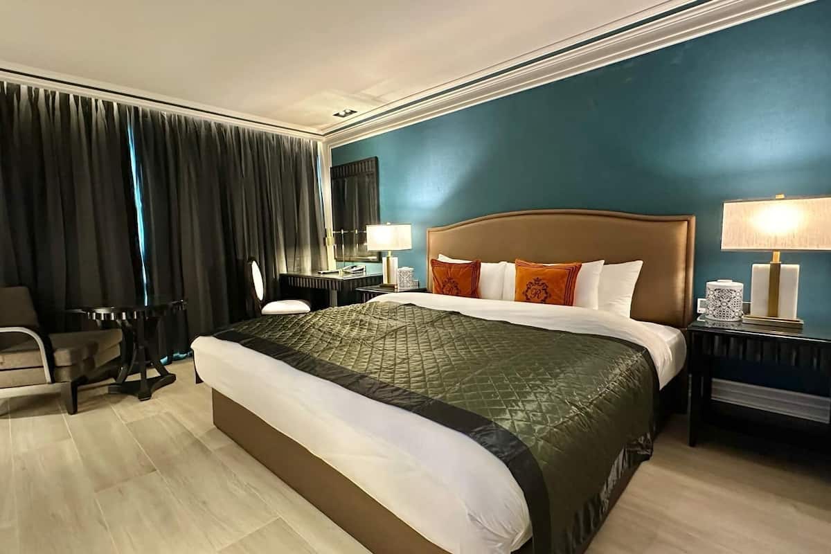 Une chambre d’hôtel avec un grand lit, une chaise, un bureau et une table de chevet avec des lampes.