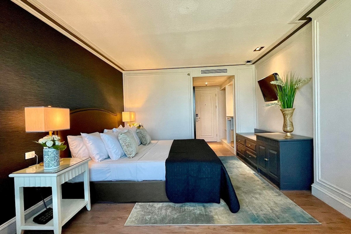 Une chambre à coucher comprenant un lit, des tables de chevet, une commode et un miroir.