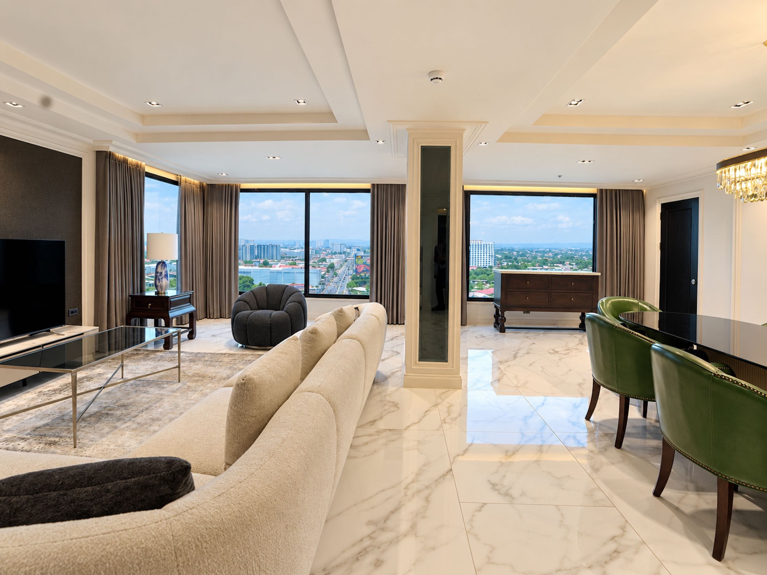 A modern living room with a large sofa, a green chair, a flat-screen TV, and a view of the city through large windows.