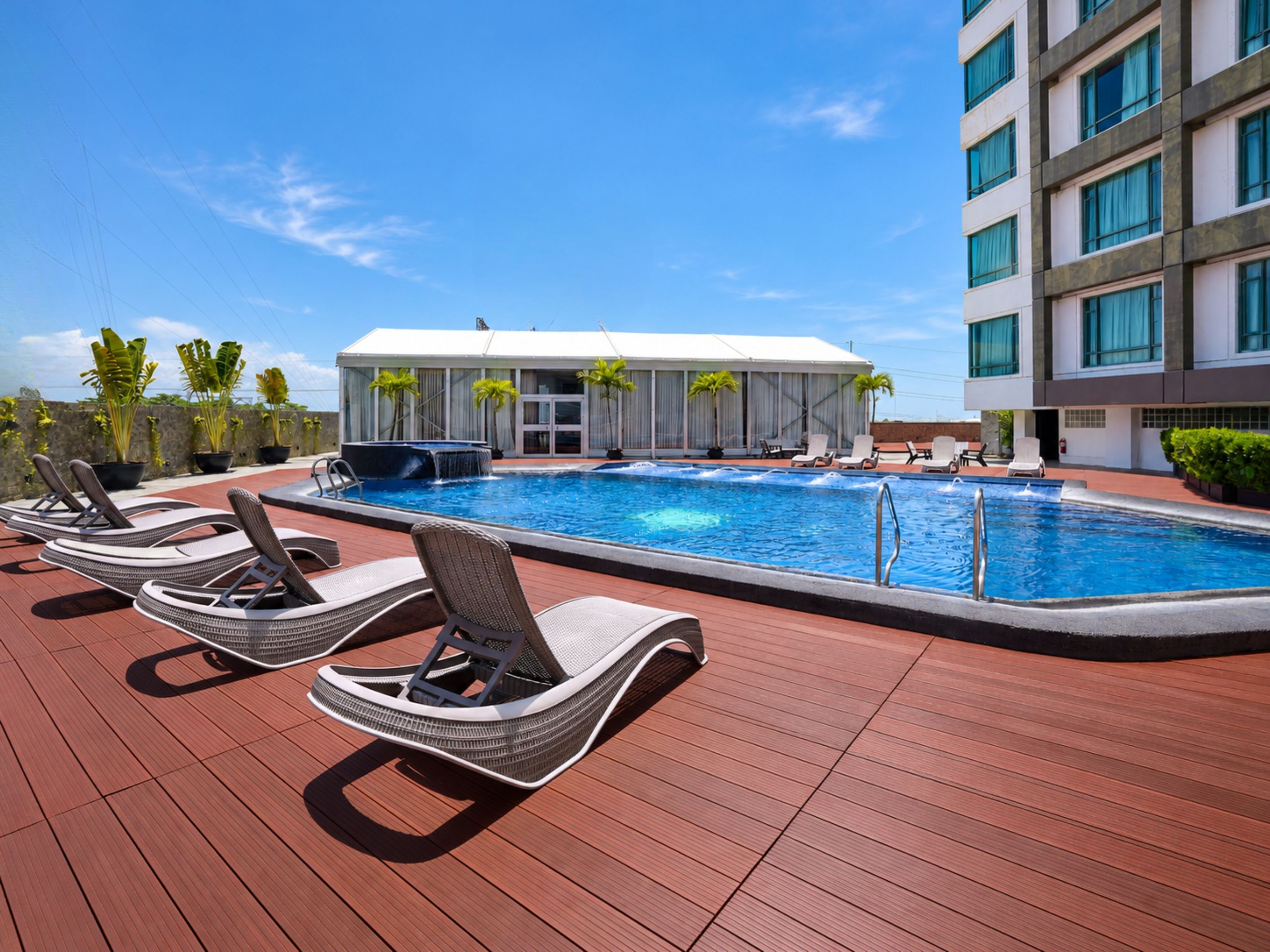 Un espace piscine avec des chaises longues, un jacuzzi et un bâtiment doté de grandes fenêtres.