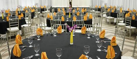 A banquet hall with round tables, each set with cutlery and glassware, and chairs with yellow napkins.