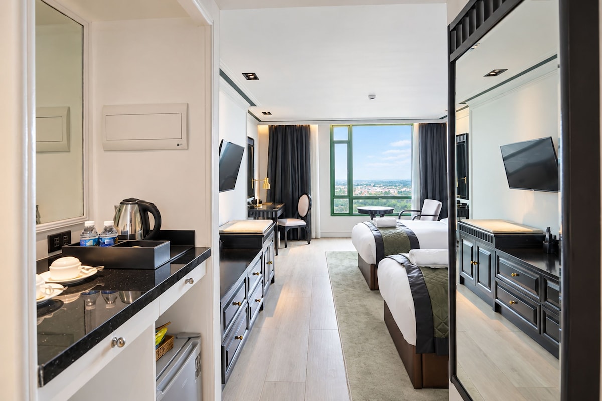 A hotel room with a bed, a desk, a chair, a television, and a large window offering a view.