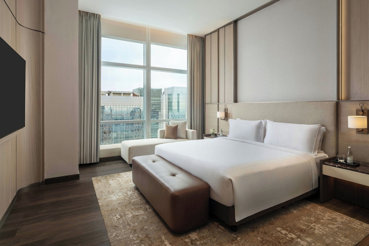 A modern hotel room with a large bed, a seating area, a TV, and a city view.