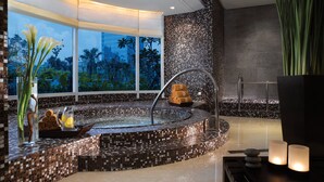 Un área de spa moderna con un hidromasaje de mosaicos, vistas a palmeras y un ventanal grande.