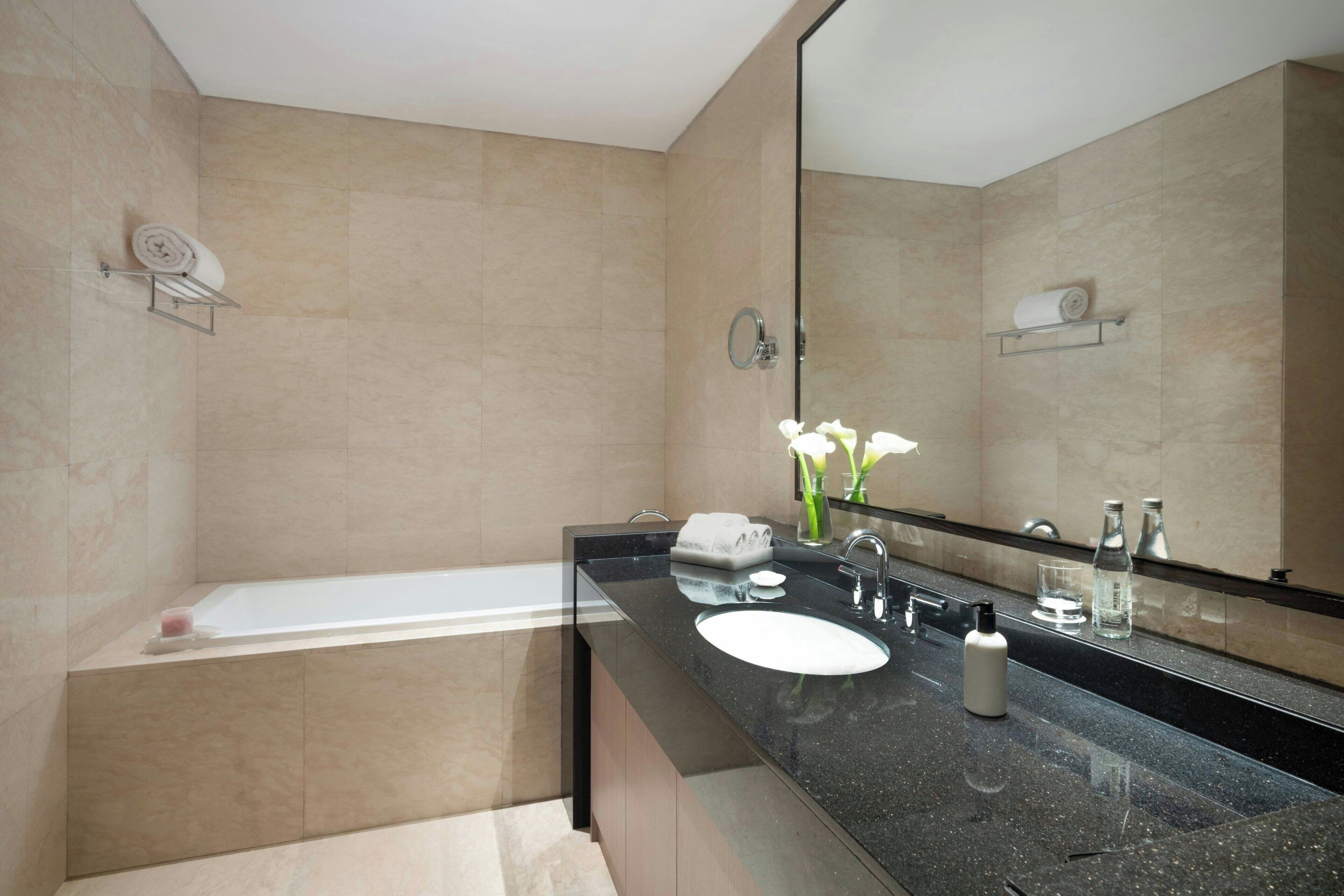 Une salle de bain moderne avec une baignoire, un grand miroir, un lavabo et un meuble-lavabo.