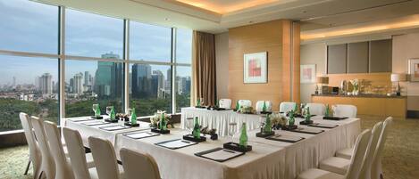 A conference room with a city view, large windows, a long table set for meetings, and a kitchenette in the background.