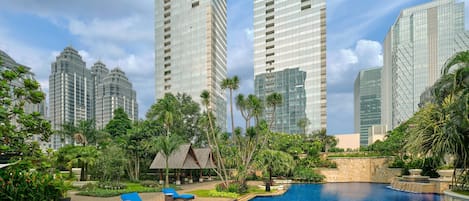 Un hotel moderno con piscina en la azotea, rodeado de vegetación exuberante y altos edificios.