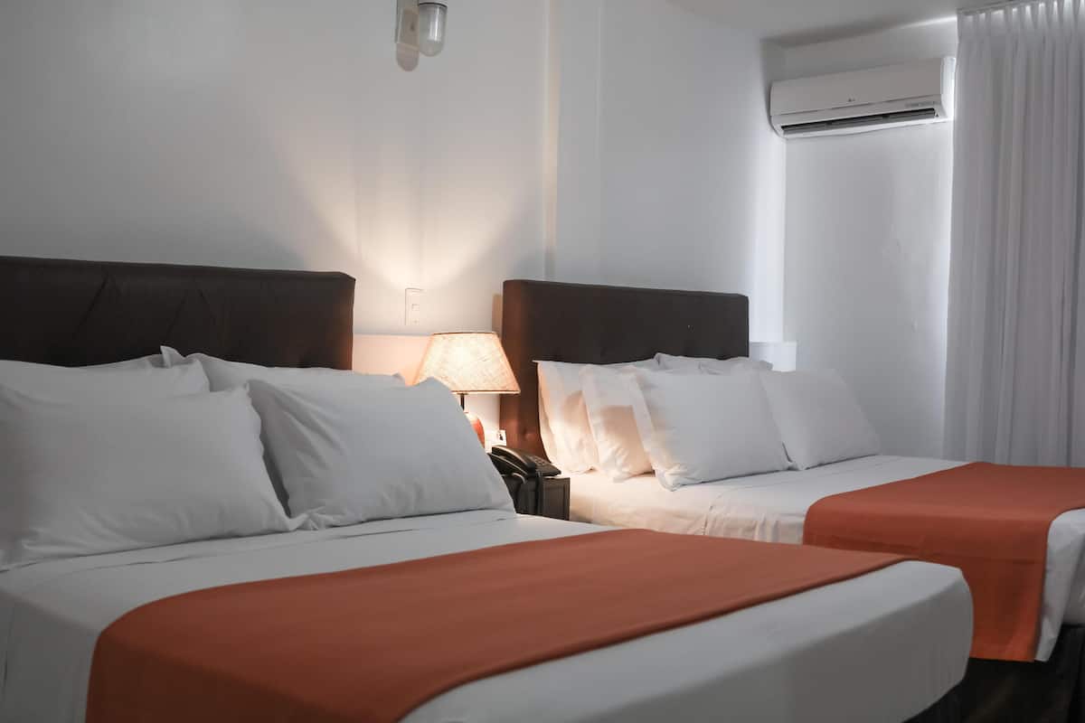 A hotel room with two beds, a lamp, an air conditioning unit, and a telephone on the nightstand.