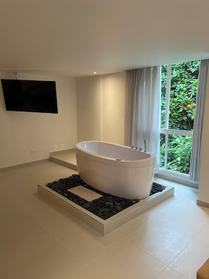 A modern bathroom with a freestanding bathtub, a large window with curtains, and a flat-screen TV mounted on the wall. - Hotel Playa Club (Cartagena)