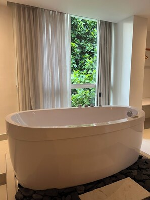 A modern bathroom with a freestanding bathtub, a window with curtains, and a view of greenery outside. - Hotel Playa Club (Cartagena)
