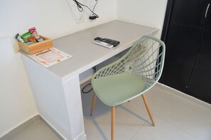 A small kitchenette with a wooden countertop, a green chair, a remote control, and a box of snacks. - Hotel Playa Club (Cartagena)