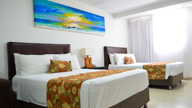 Une chambre d’hôtel avec deux lits, un tableau représentant un coucher de soleil sur l’océan et une grande fenêtre avec des rideaux.