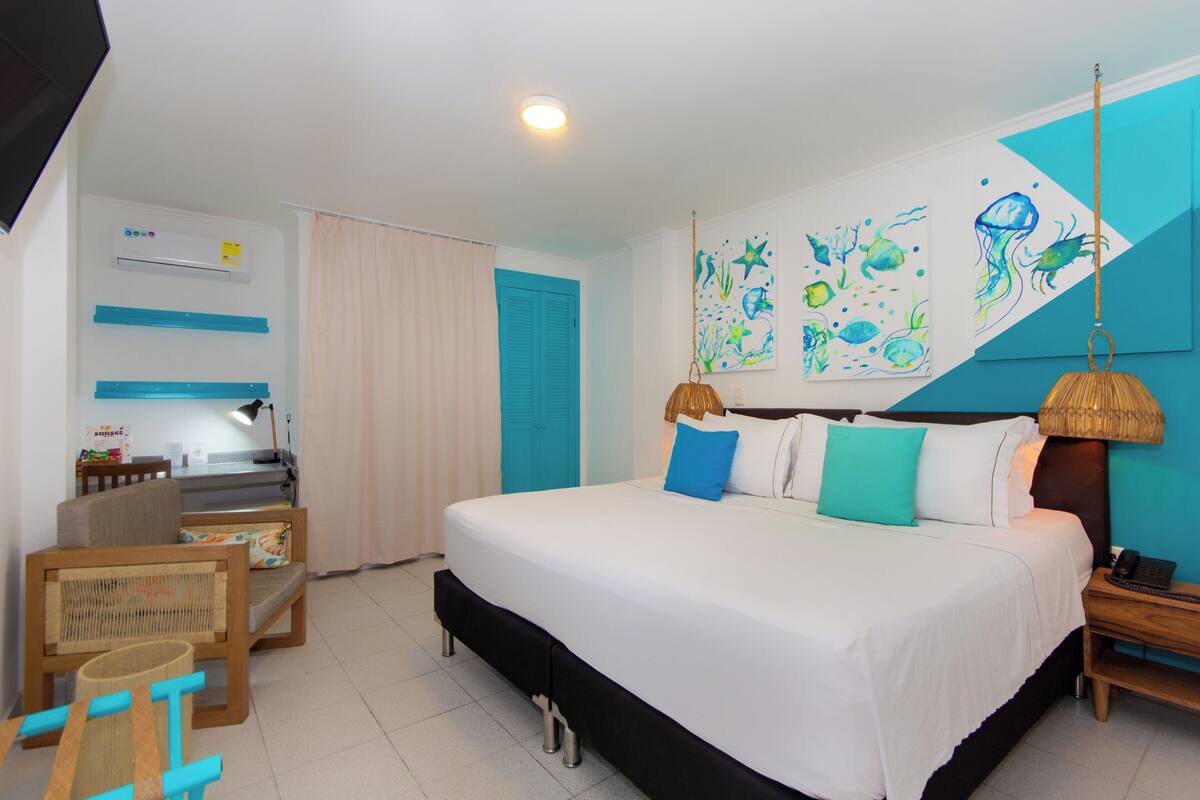 A hotel room with a large bed, a desk with a lamp, a chair, and a wall with marine-themed artwork.
