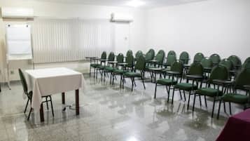 Un salón de conferencias con filas de sillas verdes, una mesa blanca y una pizarra.