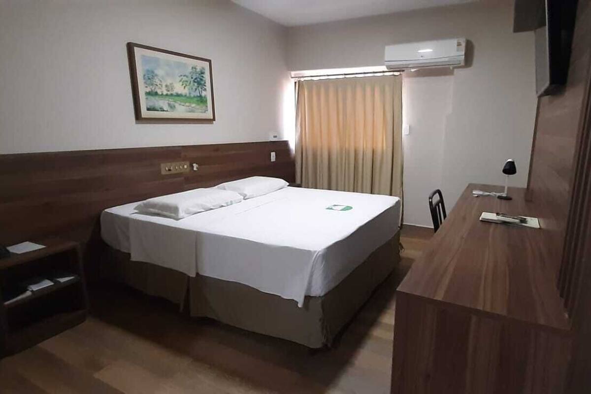 A hotel room with a bed, bedside table, and a desk with a chair.