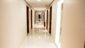 A long, narrow hotel corridor with a shiny tiled floor and wooden doors on both sides. - Hotel Vale Verde (Campo Grande)