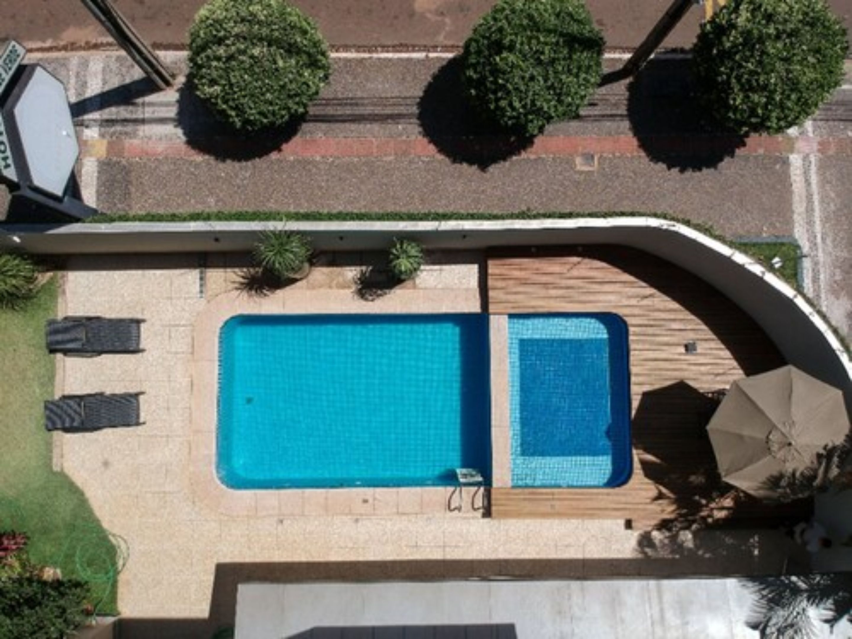 An aerial view of a swimming pool with a tiled deck, surrounded by a low wall and a curved roof structure.