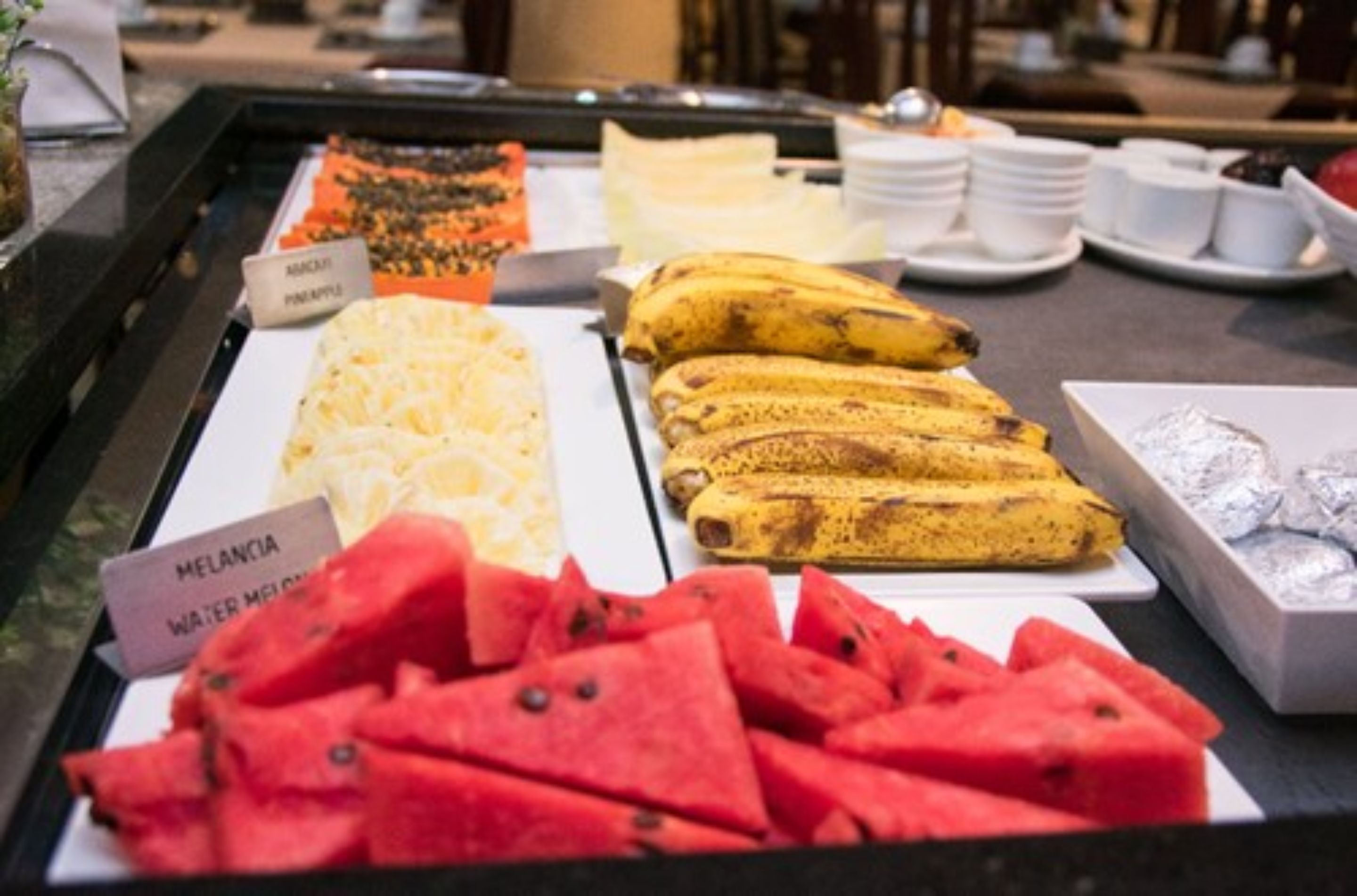 Einbufett mit beschrifteten Speisen, darunter Ananas, Banane und Wassermelone.