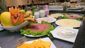 Buffet com diversos alimentos, incluindo manga, queijo e carne.