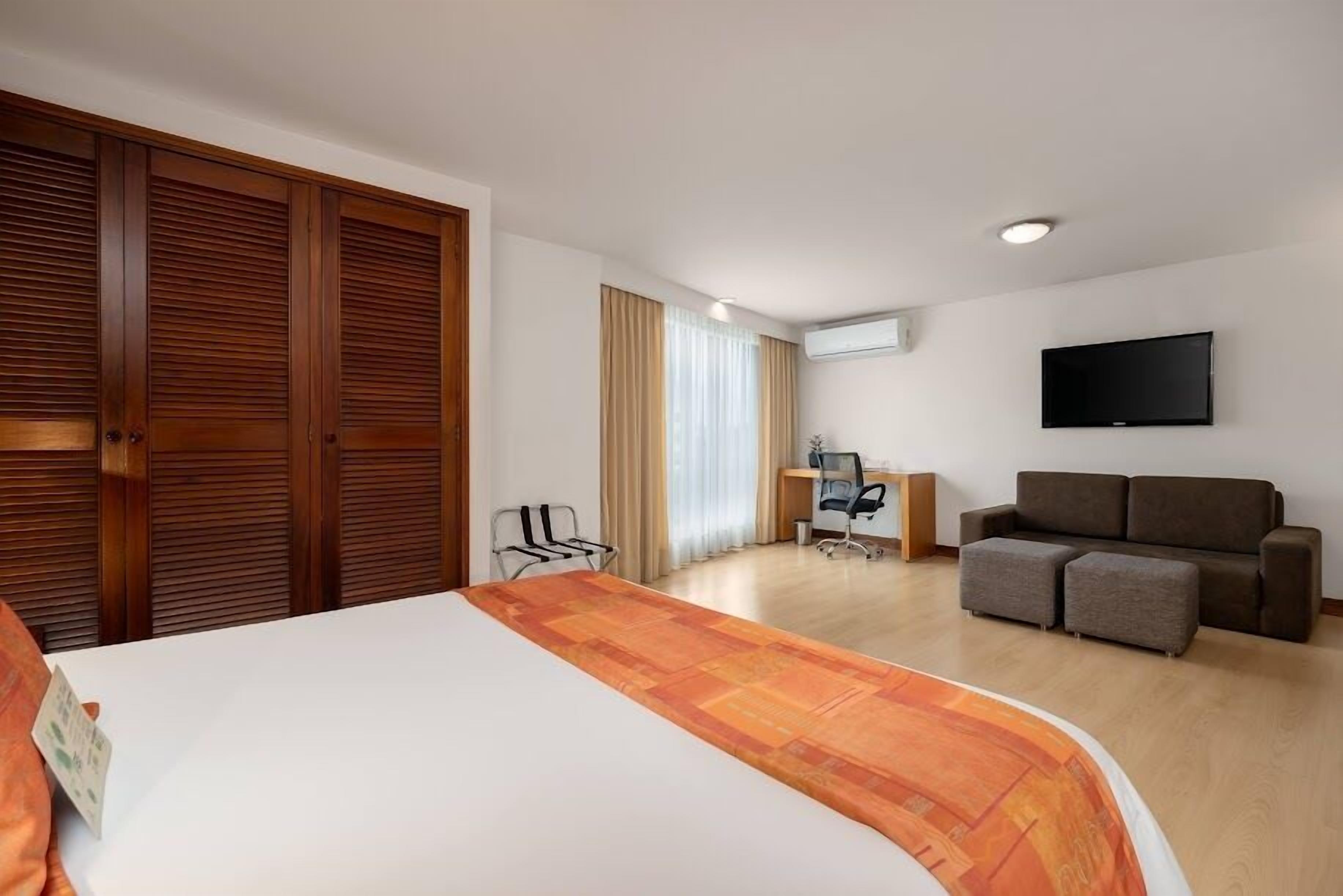 A hotel room with a large bed, a sofa, a desk, and a TV.