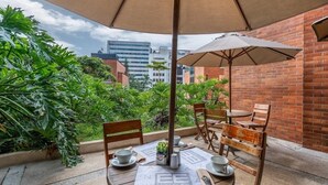 An outdoor seating area with a table set for two, an umbrella, and a view of the cityscape. - Leblón Suites Hotel Milla de Oro (Medellín)