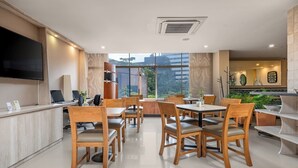 A modern dining area with wooden tables and chairs, a flat-screen TV, and a view of the city through large windows. - Leblón Suites Hotel Milla de Oro (Medellín)
