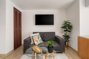 A modern living room with a grey sofa, a flat-screen TV, a glass coffee table, a potted plant, and a wooden door. - Leblón Suites Hotel Milla de Oro (Medellín)