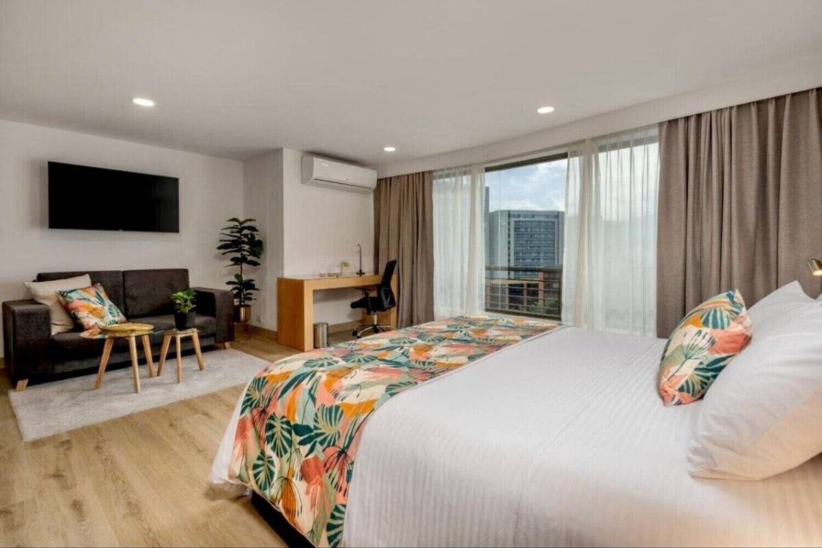 Ein modernes Hotelzimmer mit einem großen Bett, einem Schreibtisch, einer Couch und einem Fernseher.