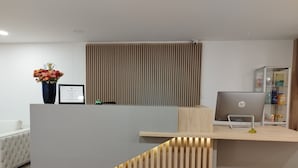Un mostrador de recepción moderno con una computadora portátil, un certificado enmarcado y un jarrón con flores.