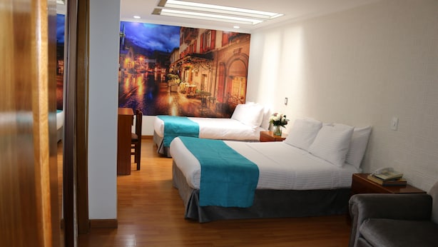 Habitación de hotel con dos camas, piso de madera, un mural en la pared y una pequeña mesa con una lámpara.