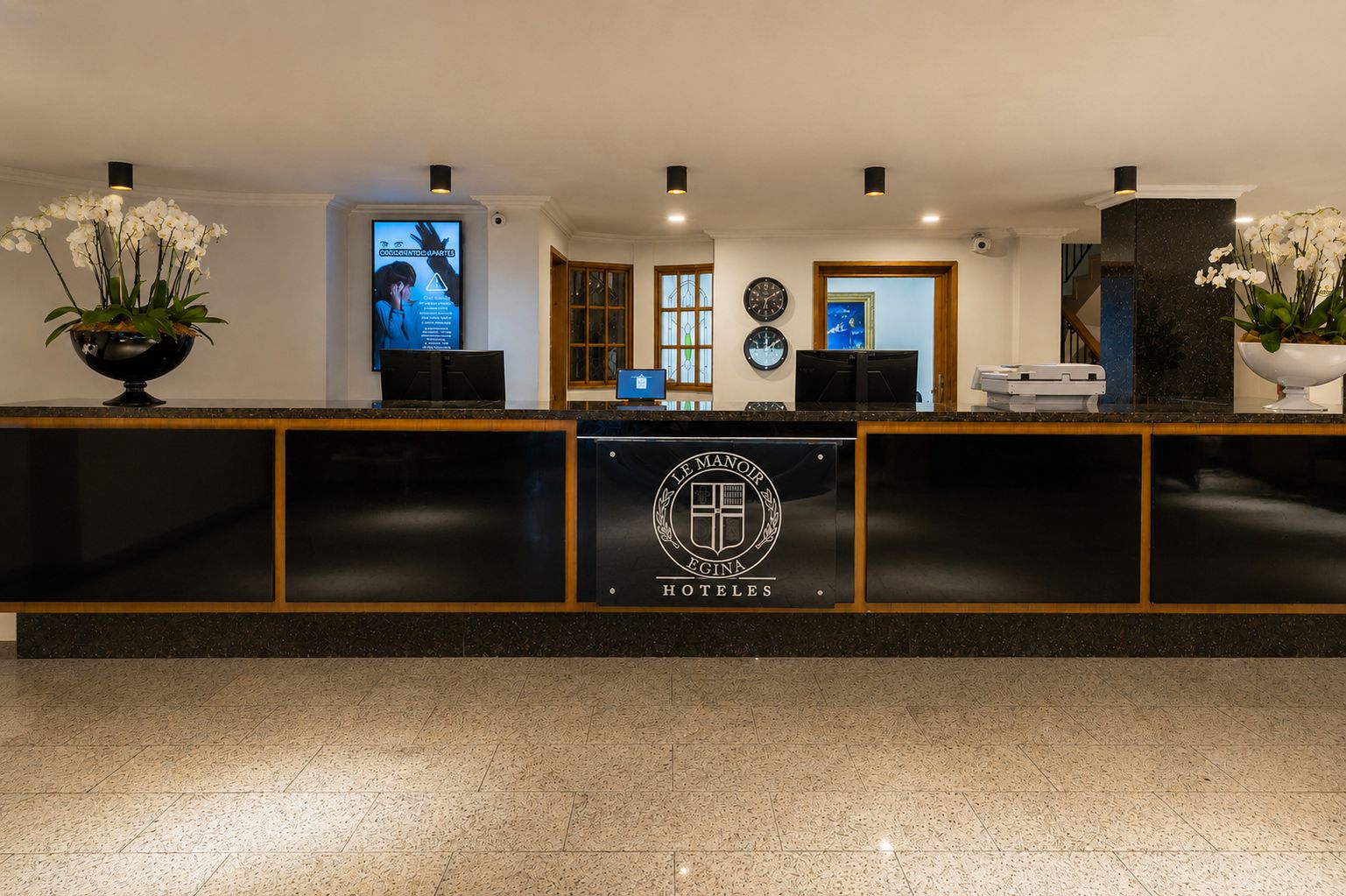 A hotel reception desk with a logo, a digital screen, and a clock.