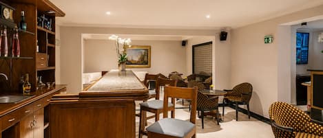 Comedor de hotel con una larga mesa de madera, varias sillas y una zona de bar con estantes.
