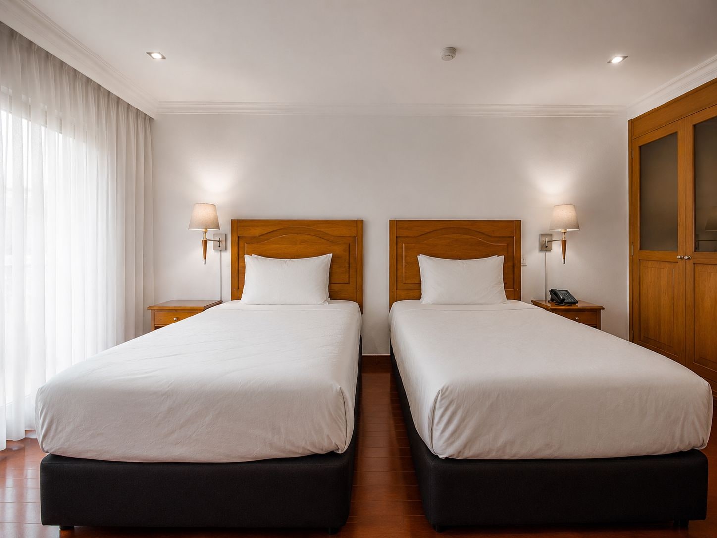 Een hotelkamer met twee bedden, elk met een houten hoofdeinde en bedlampjes.