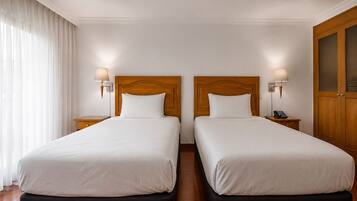 Een hotelkamer met twee bedden, elk met een houten hoofdeinde en bedlampjes.