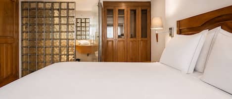 A hotel room with a large bed, wooden wardrobe, and a glass partition with a view.