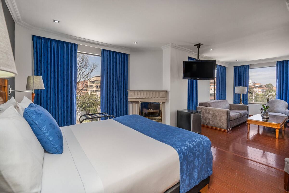 Una habitación de hotel con cama, televisión, sofá, mesa de centro y chimenea.