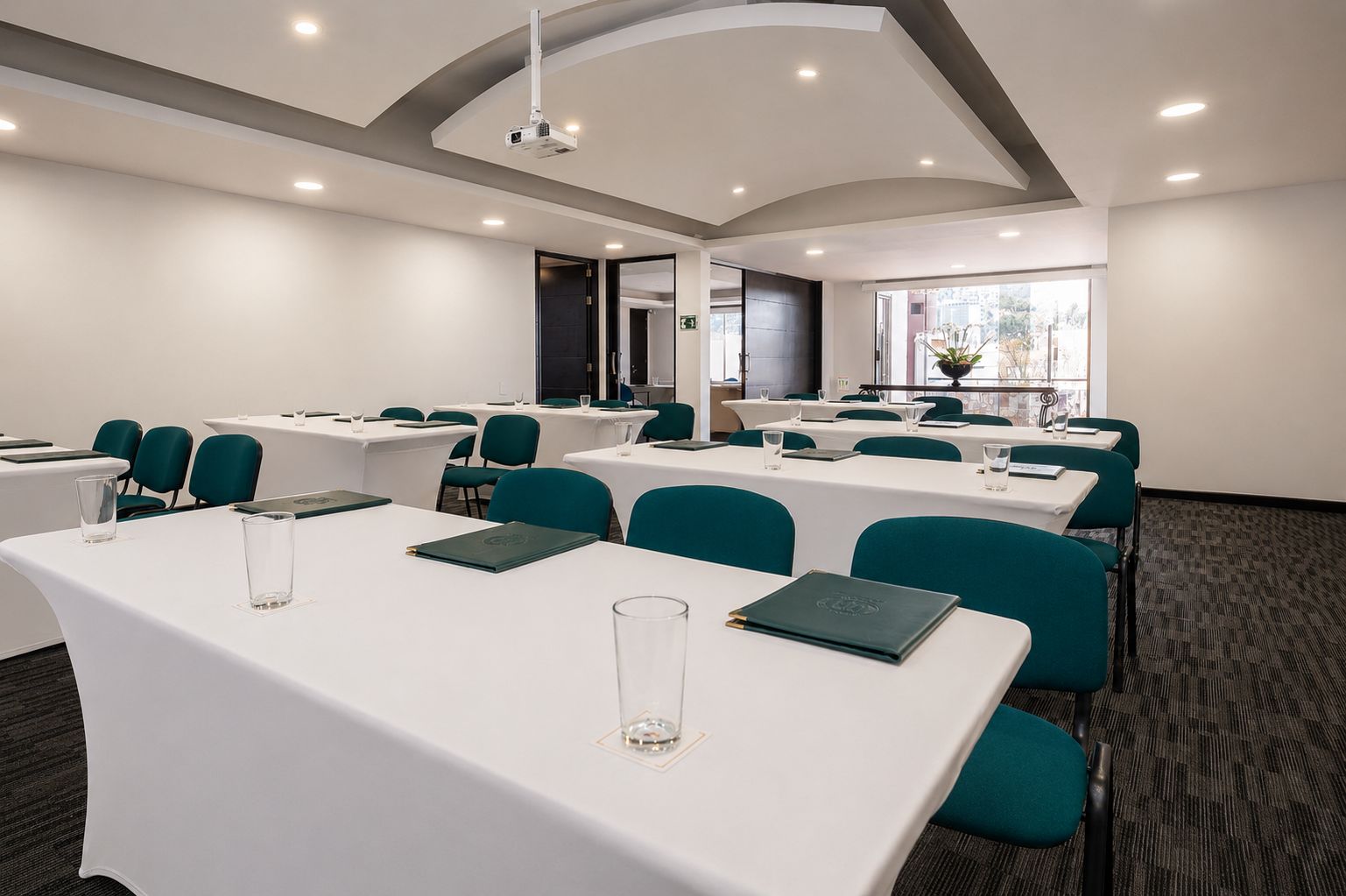 A conference room with white tables, teal chairs, and a projector.