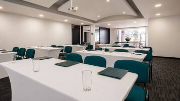 A conference room with white tables, teal chairs, and a projector.