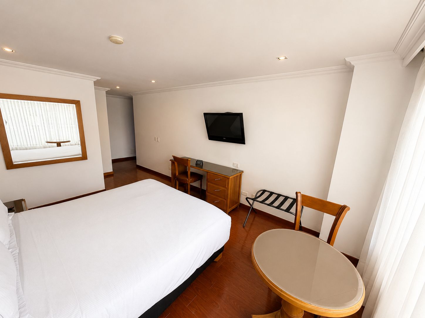 A hotel room with a bed, a desk, a chair, a television, and a window with blinds.