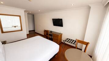 Habitación de hotel con cama, escritorio, silla, televisor y ventana con persianas.