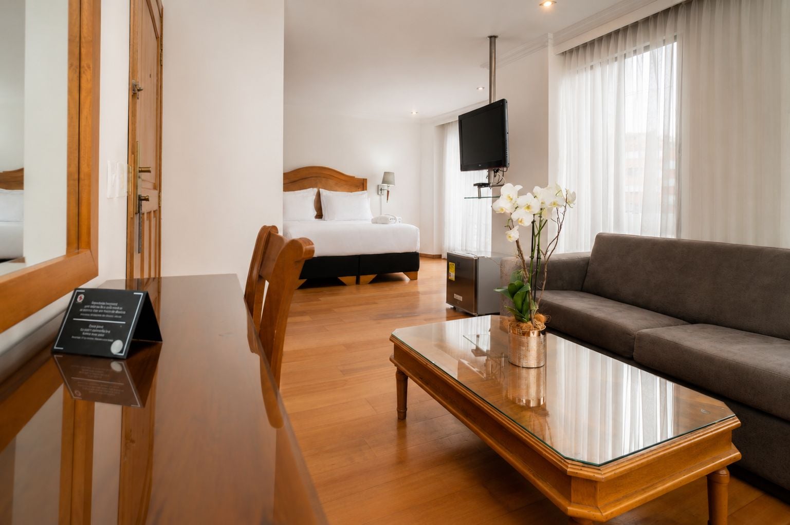 Quarto de hotel com uma mesa de jantar de madeira, um sofá, uma cama e uma TV.