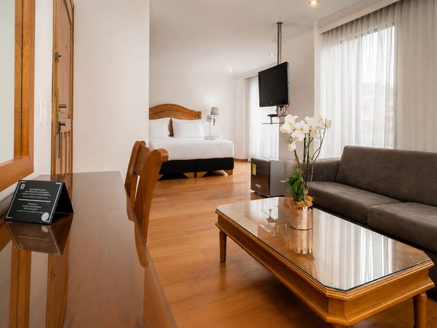 Una habitación de hotel con una mesa de comedor de madera, un sofá, una cama y un televisor.