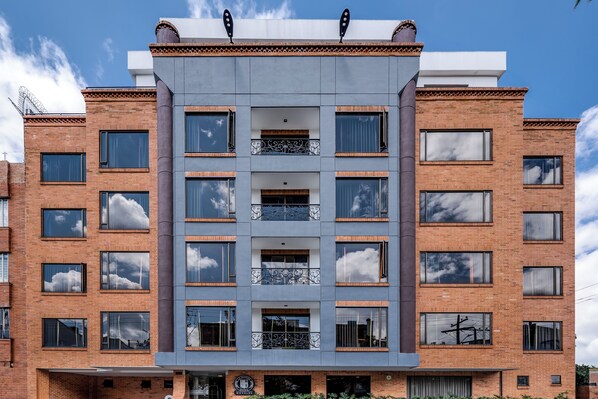 Un edificio de varios pisos con un diseño arquitectónico moderno, que presenta una combinación de fachadas de ladrillo y concreto, ventanas amplias y balcones con barandillas decorativas.