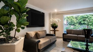 Een woonkamer met een bank, een salontafel, een grote plant en uitzicht op groen.