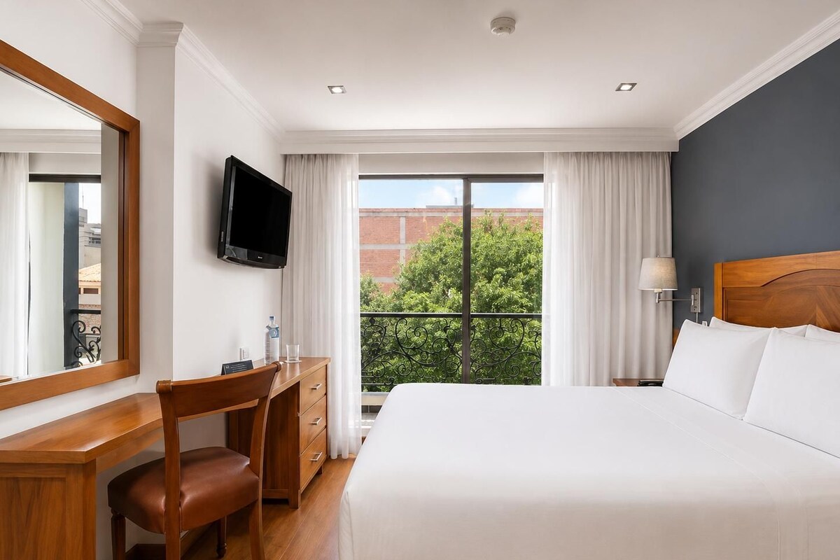 A hotel room with a bed, a desk, a chair, a television, and a window with curtains.